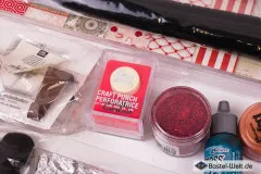 Detailausschnitt mit Craft-Punch-Motivstanze, rotem Glitter, Distress-Ink in Petrol und kupferfarbener Perlen-Farbe.